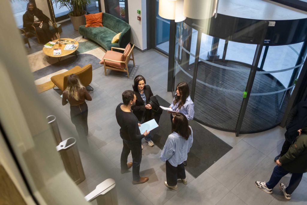4 collègues, vus de haut, discutant au milieu de l'entrée d'un bureau, de type open space