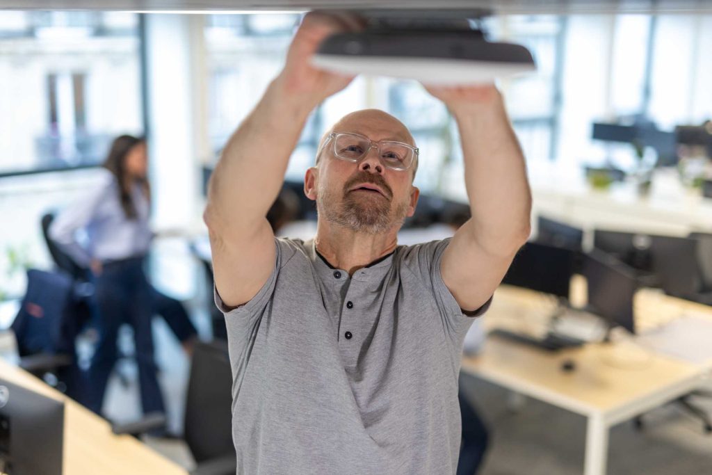 Homme réparant un luminaire dans un open space